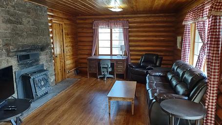Log cabin living room with stone fireplace, couch, chair, desk, coffee table and end table.