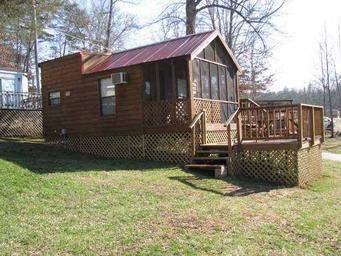 Exterior view of a rustic cabin on a raised deck with steps and surrounding grounds — represents the campground's cabin rental accommodations.