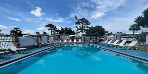 Heated outdoor pool lined with lounge chairs and flag pole at Palm View Gardens RV Resort site.
