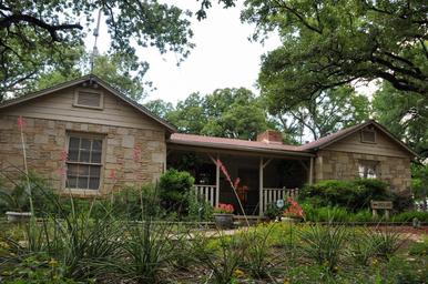 Stone building (office/stone house) set among mature oaks and landscaping — shows on-property architecture and shade character referenced on the site.