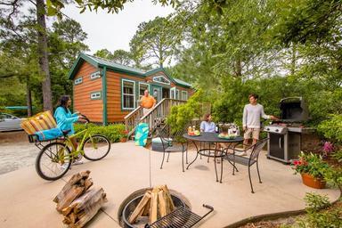 Photo of a cabin/lodge patio area with grill, table and fire pit — represents on‑site lodging amenities and outdoor campsite living (used on the page’s lodging imagery).