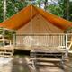Front view of a raised canvas glamping/tent cabin with deck and picnic table in a wooded setting — matches the KOA ‘glamping’/cabin accommodations shown on the campground’s ways-to-stay photos page.