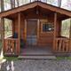 Exterior of a rustic cabin labeled with a name plate, front porch and picnic table — good for showing cabin rentals (source: Cabins / Rental page).