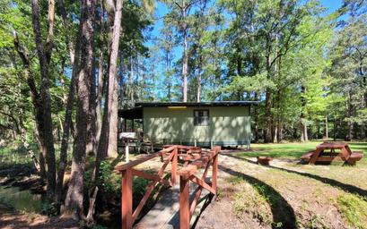 Cabin exterior with small footbridge and picnic table beside a creek/pond — good view of cabin lodging and grounds. Sourced from the site’s campground/cabin photos.