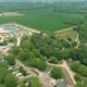 High-angle aerial view showing the campground layout: pool/pond with beach, RV rows, roads and wooded river corridor — suitable overview and matches homepage hero image on property site.
