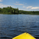 Yellow kayak on a blue lake with a tree-lined shore and cloudy sky in the distance