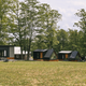 Wide shot showing several cabins spread across an open grassy area with trees — gives an overview of cabin cluster and grounds, helpful for a property gallery.