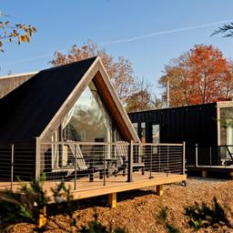 Close exterior photograph of a modern A-frame style cabin with deck and landscaping — corresponds to the cabins described on the main site and ‘Ways To Stay’ content.