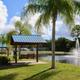 High-resolution exterior view of the property pond with fountain, shaded benches and RV pads visible in the background — from the site’s community page illustrating on-property landscaping and water feature.
