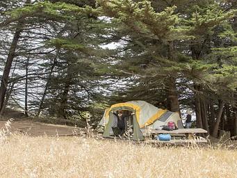 Two people set up a large tent near a picnic table at Site 3.