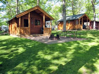 Photo showing two cabin units with picnic tables and fire ring area — useful to represent cabin lodging options on the grounds.