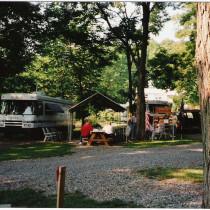 Close campsite view showing RVs, gravel drive, picnic table and shade trees — good representation of typical site and grounds; from the Campground Amenities page.