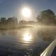 A boat is floating on a river with the sun shining through the fog