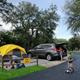 Tent area with a pitched tent in a fenced pad, adjacent parking, paved roads and family activity — useful for showing tent camping spaces and family-friendly grounds.