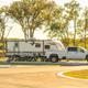 Ground-level photo of an RV and tow vehicle parked on a concrete pad beside landscaping — shows typical guest site setup and amenities.