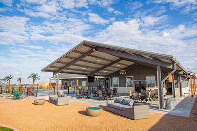 Outdoor patio area with seating, tables, and a large covered structure near a playground and a swimming pool, under a partly cloudy sky.