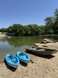 Kayaks and a jon boat on the sandy beach of the stocked lake, swim platform beyond