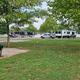 Wide panorama showing RVs, grassy common area, picnic/BBQ grill and mature trees — useful for showing campground amenities and spacing (from the park’s photo gallery).