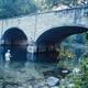 a man in a river fishing underneath a bridge
