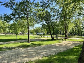 Open campground area with multiple gravel RV/campsite pads, picnic tables and mature trees — good overall view of site layout and grounds (used as site social image on the property page).