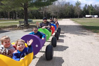 Colorful barrel-train ride with guests on a campground road — depicts an on-site recreational activity described on the property page.