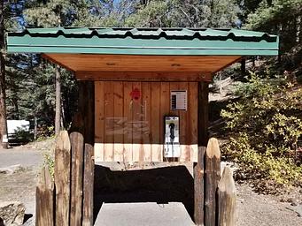 A payphone located underneath a  wooden kiosk with a green metal roof.