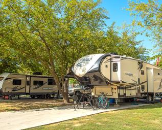 RV site with large fifth-wheel trailers, paved pad and shade trees — clearly shows RV accommodations and site layout on the property (from the resort’s website).
