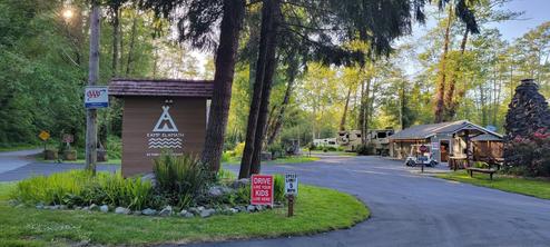 Entrance/office area with Kamp Klamath sign, kiosk and surrounding grounds — useful for orientation and arrival impression; from the amenities/landing page.