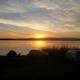 Sunset view across the lake from the RV Park area showing parked cars, a tent and shoreline — matches the RV Park page on the site and illustrates campsite/lakeside camping on the property (source: /rv-park).