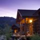 Evening exterior view of log cabins on the property with lit windows and surrounding hillside — good atmospheric photo of lodging cabins and grounds.
