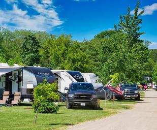 Row of RV sites with vehicles and hookups along a campground road, showing site setup and spacing — supports ‘Sites & RVing’ section imagery.