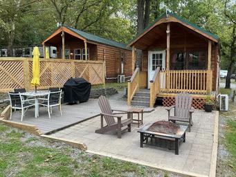 Two cabins with porches, outdoor furniture and paved patio area — clear photo of available cabin accommodations and appears in the campground’s 'ways to stay' gallery.