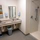 Dorm bathroom featuring one large shower, two sinks, two mirrors, two soap dispensers, and a trashcan. 