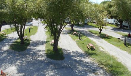 Ground-level view of tree-lined RV pads with picnic tables and hookups — useful campsite detail and feel of the grounds (gallery page).