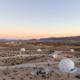 Aerial/landscape shot showing scattered geodesic domes across the desert at sunset — good overview of campsite distribution and environment (source page: Accommodations).