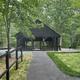 Paved walkway leading to a wooden roofed and paved picnic pavilion shaded by trees