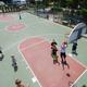 Aerial/angled view of a full basketball court with players and RVs visible in the background — shows courts, active use, and proximity to RV parking/campsites; sourced from the property’s photo gallery.