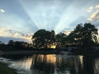 Wide shot of the on‑site reflecting/stocked pond with fountain at sunset and campground trees/cabins in background — matches the site background image and highlights a key on‑site amenity.