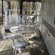 White metal patio table and chairs on a screened porch beside a trailer wall and railing.