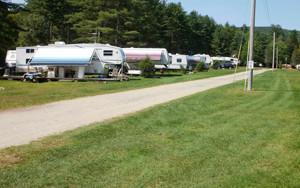 Row of RVs/trailers along a gravel road with grassy sites and utility hookups visible — shows the campground’s RV/trailer pitch area from the gallery.