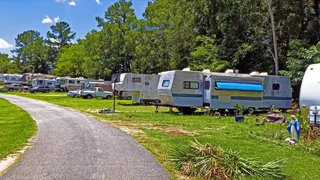 Side-angle ground-level view showing a line of trailers and grassy lots with trees — shows campsite spacing and vegetation on the grounds (from the park website).