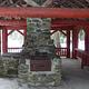 Stone fireplace and chimney next to counter under red-painted log shelter.