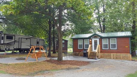 Deluxe cabin with adjacent RV visible, showing cabin exterior, patio and paved site area — demonstrates cabin accommodations offered at the KOA (ways to stay photo).