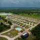 High, wide aerial view showing the entire resort layout: RV pads in rows, the pool, pond, roads and surrounding landscape. Source page (RV sites) matches property and confirms it's an on-site drone shot.