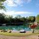 Panoramic view of the on-site pond with paddle boats, life jackets and surrounding beach/shore — excellent overview of a primary campground feature; appears on the Activities page and as a site photo. 