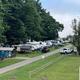 Campground scene with RVs, trees, and a dirt road.