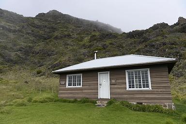view of cabin surrounded by grass and tall cliff behind