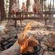 People sitting by a campfire at a picnic table in a pine forest