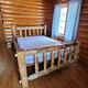 Log bed in log cabin with wood floors and log walls and wood ceiling. 