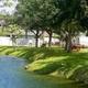 Grassy pond edge with picnic benches and residences visible across the water — highlights on‑grounds water feature and relaxing lakeside seating.